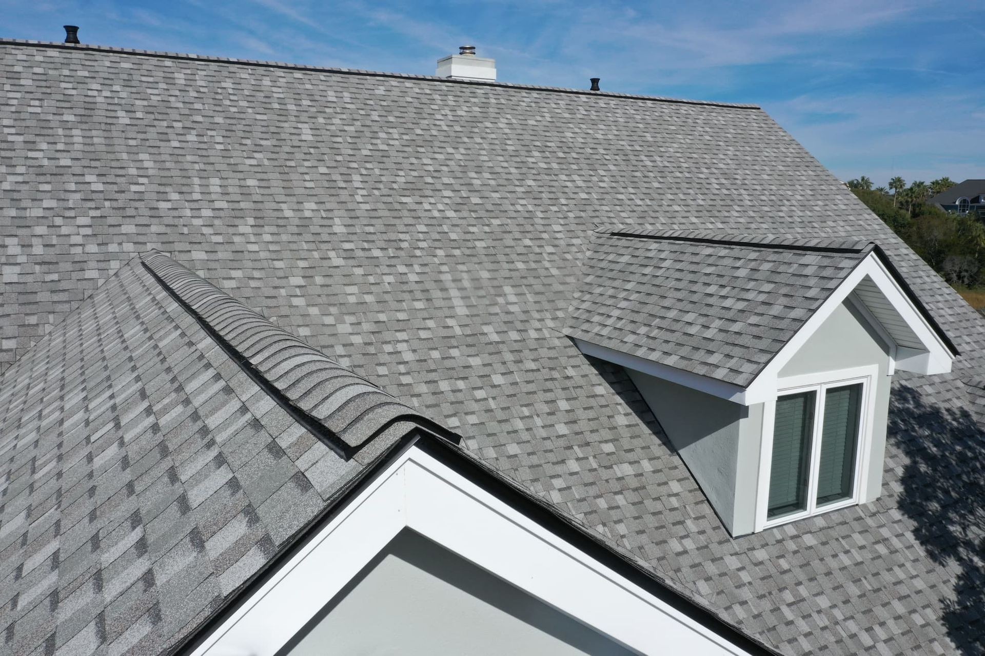 Close-up view of a residential roof with grey asphalt shingles and a small dormer window.