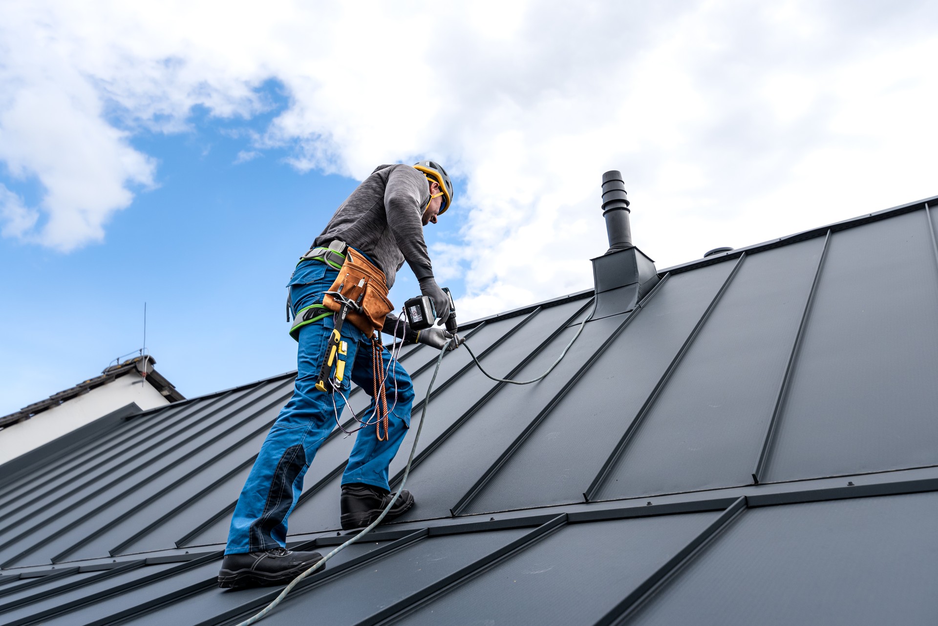 Work at heights. A roofer with tool belt and save harness climbing to the top of the roof.