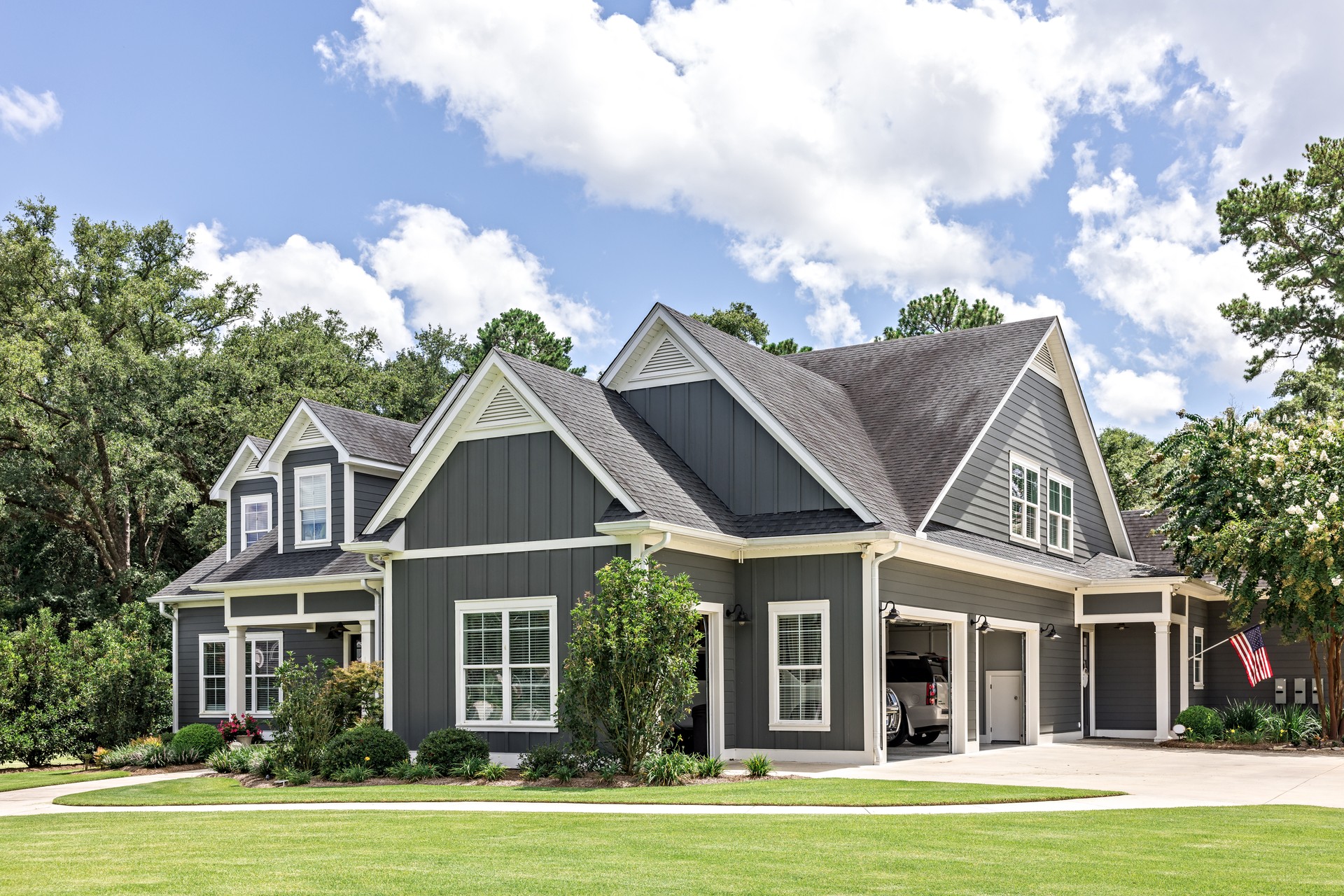 A large gray craftsman new construction house with a landscaped yard and leading pathway sidewalk